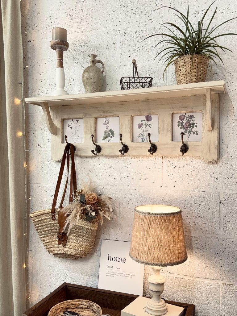 Vue d’ensemble d’une étagère murale en bois avec cinq crochets et quatre cadres décoratifs.
